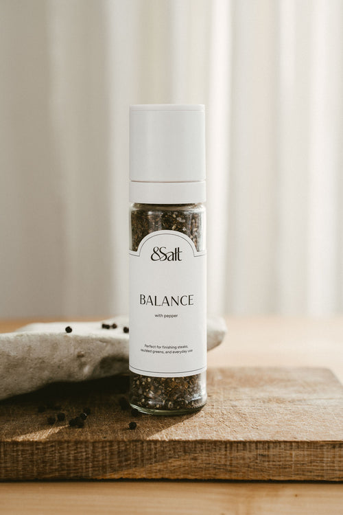 Spice grinder labeled 'Balance' by &Salt on a wooden surface with a neutral background