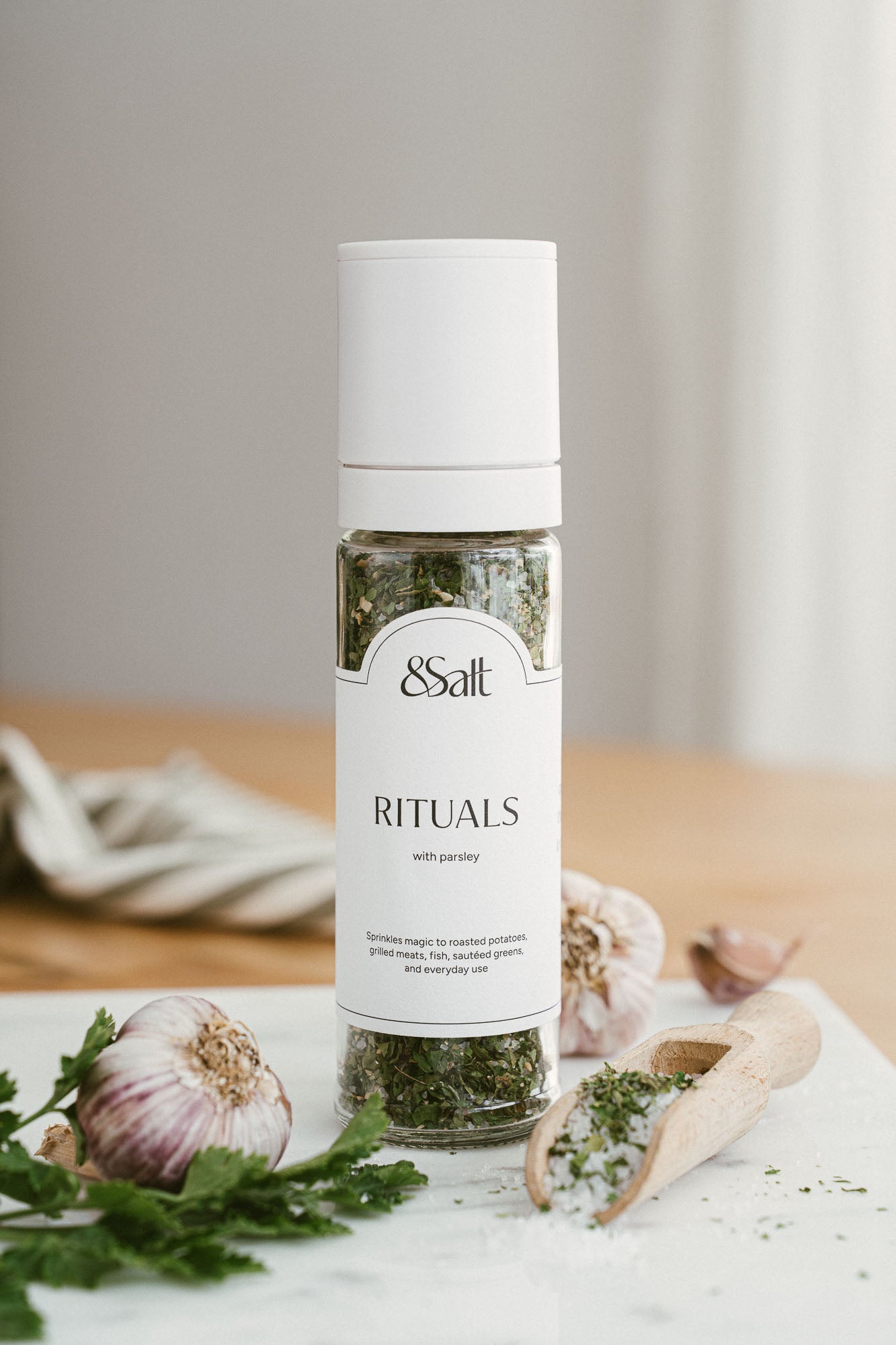 White salt grinder on a wooden surface with herbs and garlic.